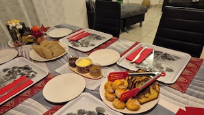 A dining table set with plates, cutlery, and food items, including bread and pastries, with a patterned table runner and a vase of flowers.