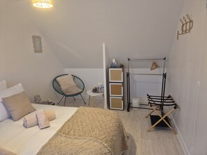 Un dormitorio con cama, una silla, una mesita, una estantería y un tendedero.