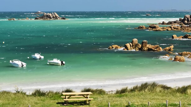 A coastal scene with clear turquoise waters, boats, and rocky outcrops.