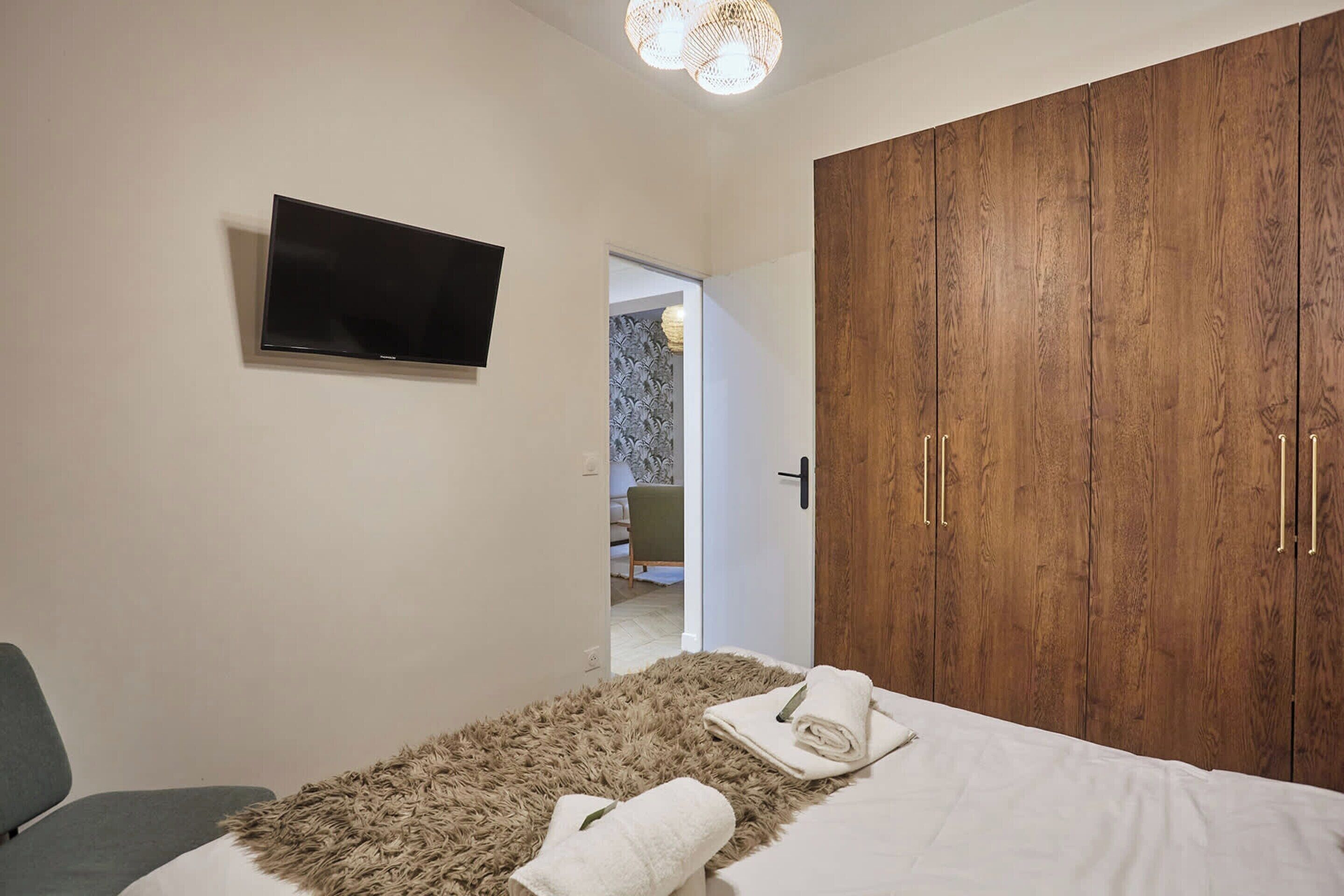 A bedroom with a bed, a television, a wardrobe, and a door leading to another room.
