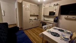 A compact kitchen with white cabinets, a microwave, and a dining area set with plates and glasses. - Apartament In Style (Łódź)