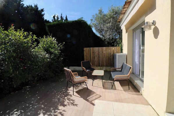 An outdoor patio area with wicker furniture, a wooden fence, and a window with blinds. - Bright House - AC - 2br-4p - Gassin (Gassin)