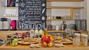 Un buffet de petit-déjeuner est mis en place, accompagné d’un panneau indiquant le menu, qui comprend du lait, du café, du pain, des fruits, ainsi qu’une mention de l’auberge et du campus.