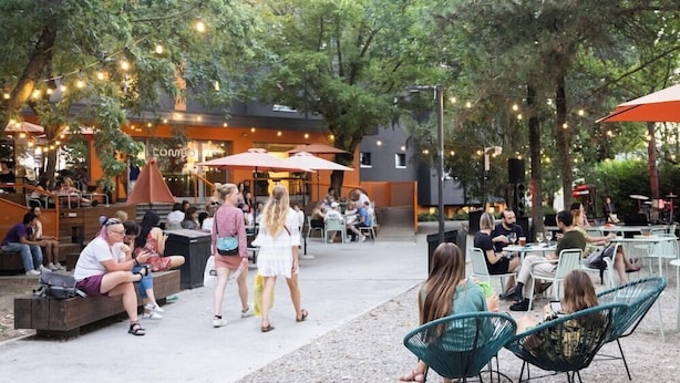 Un espace extérieur aménagé avec des tables et des chaises, entouré d’arbres et illuminé de guirlandes lumineuses.