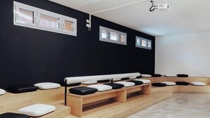 Une pièce avec un mur noir, des bancs en bois dotés de coussins et un projecteur au plafond.