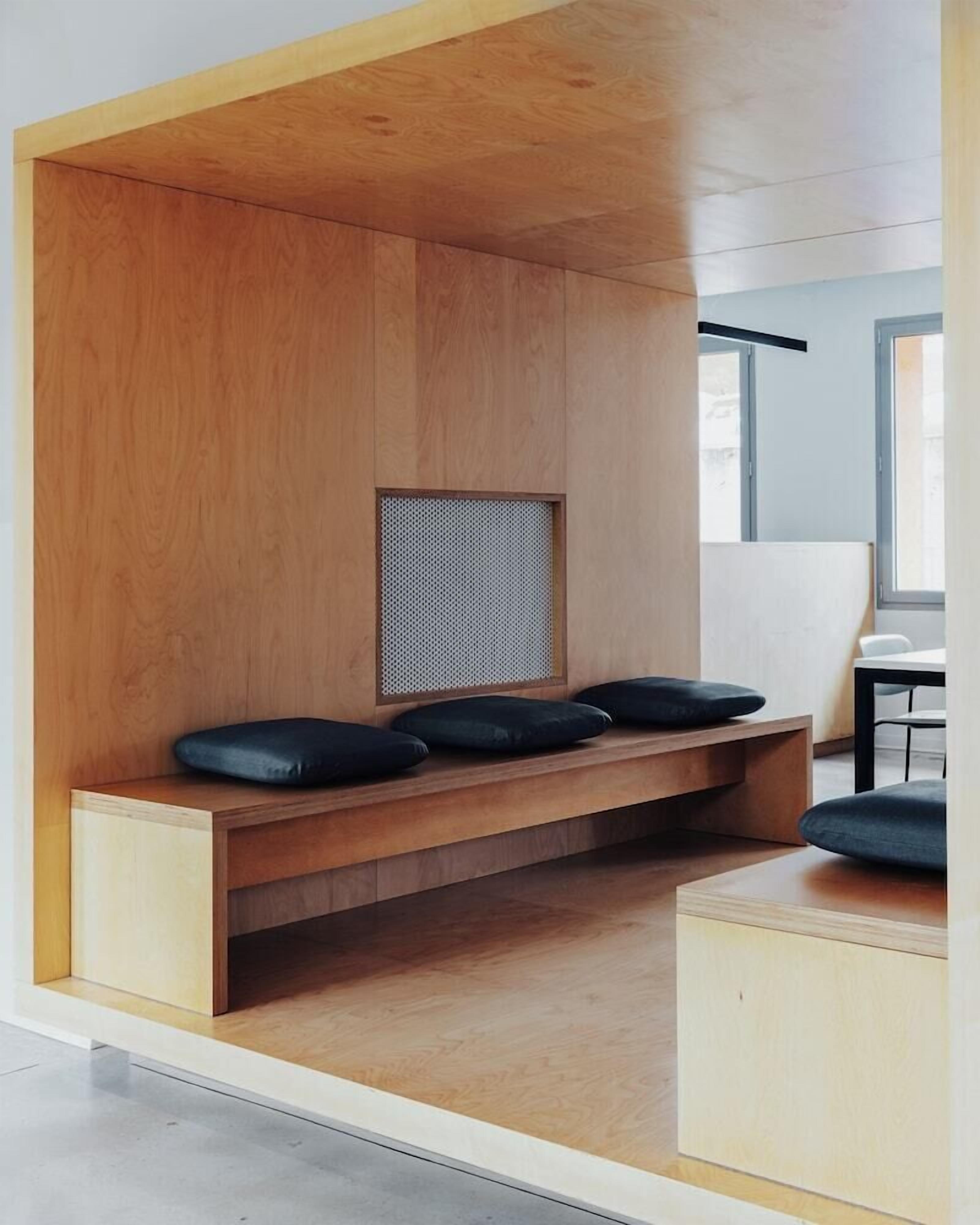 Un espace de détente moderne et minimaliste, avec un banc en bois et des coussins, une petite fenêtre et une vue sur la pièce adjacente.