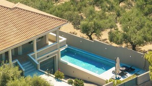 Een modern huis met een zwembad, een overdekt terras en uitzicht op olijfbomen.