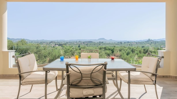 Een terras met tafel en stoelen, met uitzicht op een mooi landschap met heuvels en groen.