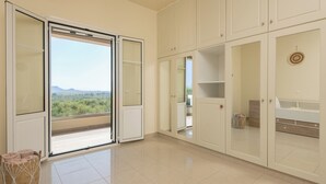 Een ruime kamer met een grote schuifglasdeur naar een balkon, witte kasten en een betegelde vloer.