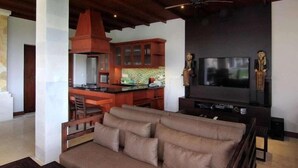 Una sala moderna con un sofá, un televisor y una cocina al fondo.