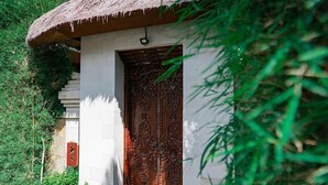 Un edificio tradicional con una puerta de madera grande y ornamentada, rodeado de abundante vegetación.