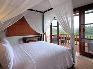 A bedroom with a large bed, a wooden headboard, and a view of a balcony with outdoor furniture. - Uma Stana Villa (Ubud)