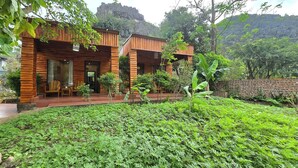 Een houten chalet met terras, omringd door weelderige begroeiing en een bergachtig achtergrond.