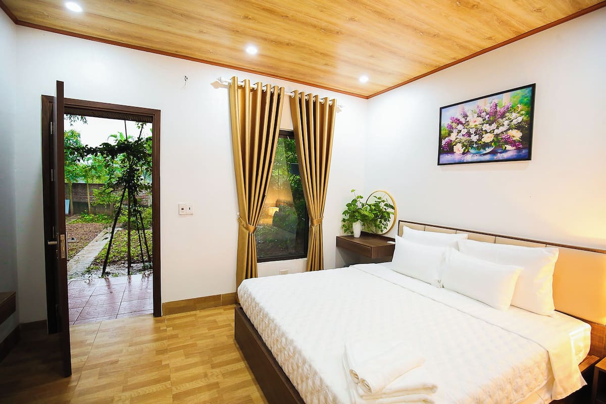 Una camera da letto con un letto, tende, un quadro e una pianta in vaso.