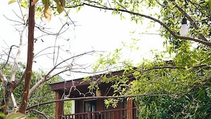 Een houten gebouw met een balkon dat uitkijkt over een vijver, omringd door weelderige begroeiing en kleurrijke bloemen.