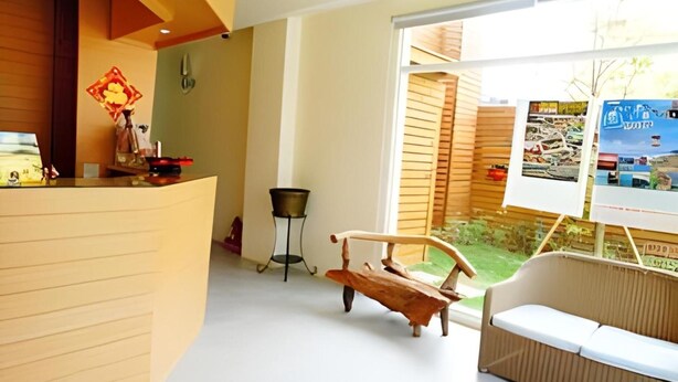 A reception area with a wooden reception desk, a small table with a basket, a wooden bench, and a white sofa. - Sasa Nor Lamour B B (Hengchun)