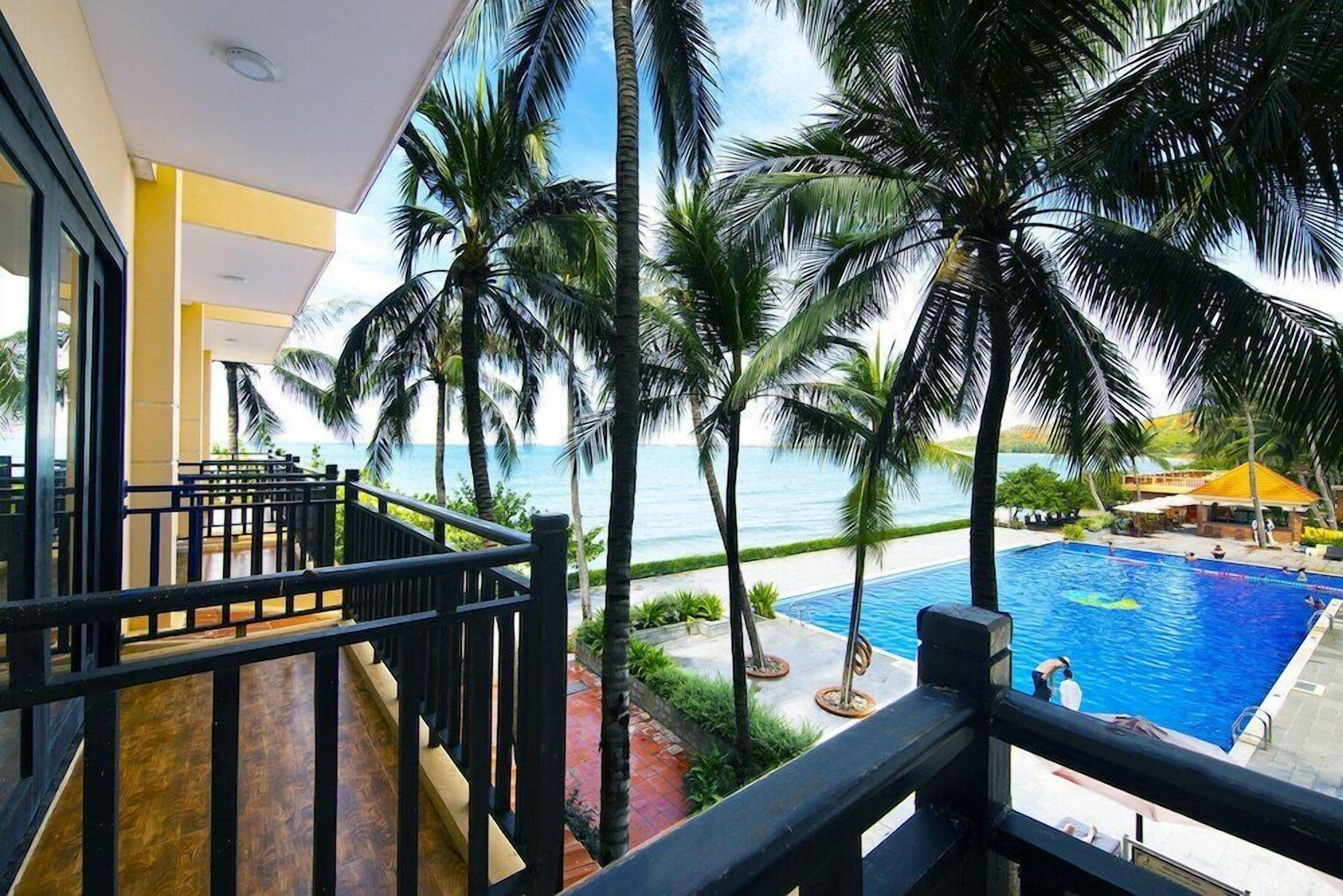 A poolside view with a clear view of the ocean, palm trees, and a swimming pool.