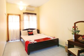 A bedroom with a bed, a bedside table, a mirror, and a window with curtains. - Hon Rom 1 Resort (Phan Thiet)