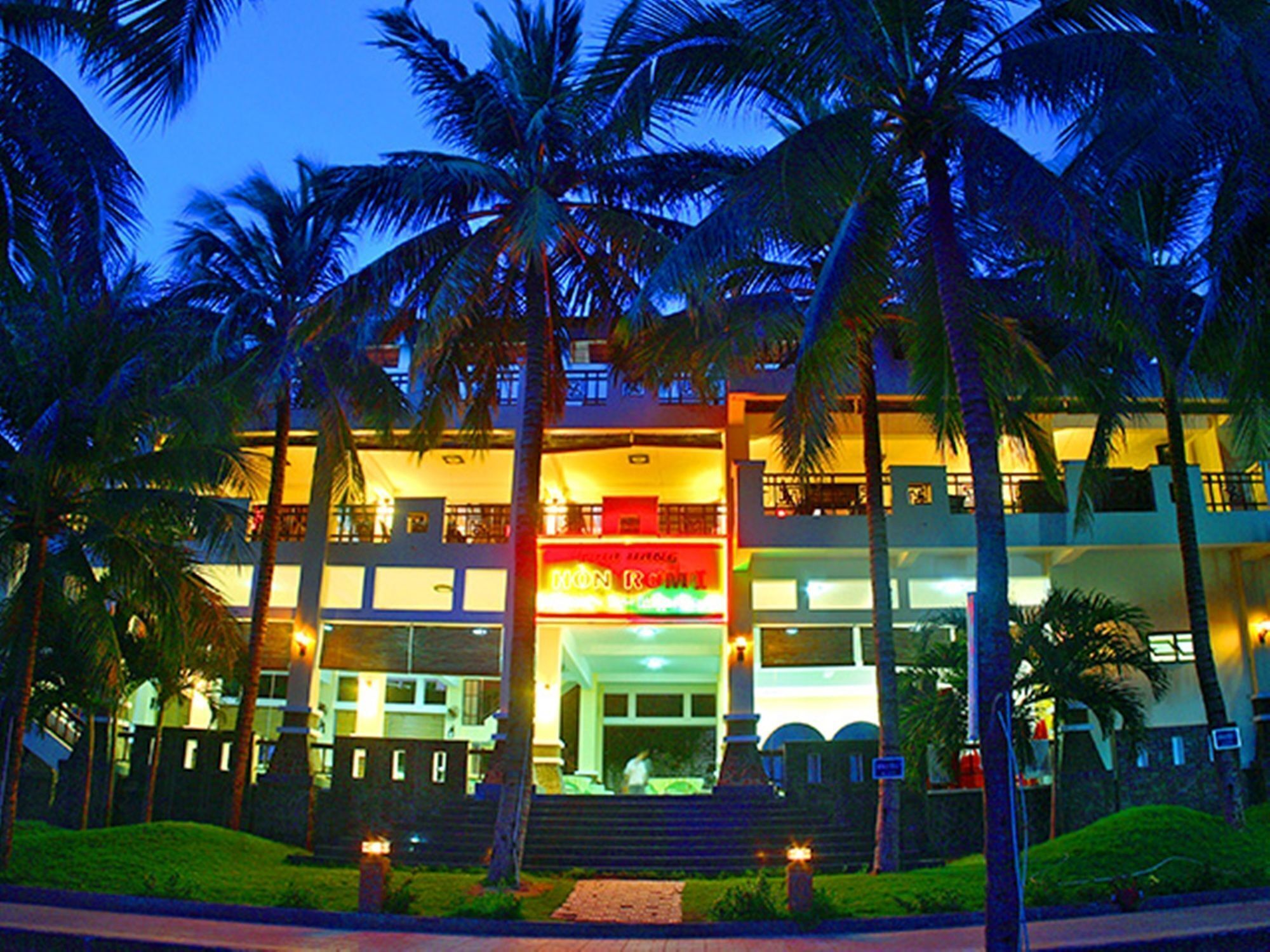 A multi-story hotel with a prominent red sign at the entrance, palm trees, and a well-lit facade.