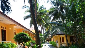 A courtyard with a pathway, palm trees, and a yellow building with a tiled roof. - Hon Rom 1 Resort (Phan Thiet)