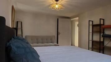 Une chambre à coucher comprenant un lit, une lampe de chevet, un luminaire au plafond et une porte donnant sur une autre pièce.