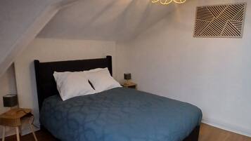 Ein Schlafzimmer mit schrägverdeckter Decke, einem Bett mit dunklem Kopfteil, einem kleinen Nachttisch mit Lampe und einer dekorativen Leuchte.