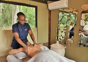 A massage therapy session in a room with a view of trees, a wall-mounted mirror collection, and a woven basket. - Nibela Lake Lodge (KwaNibela)
