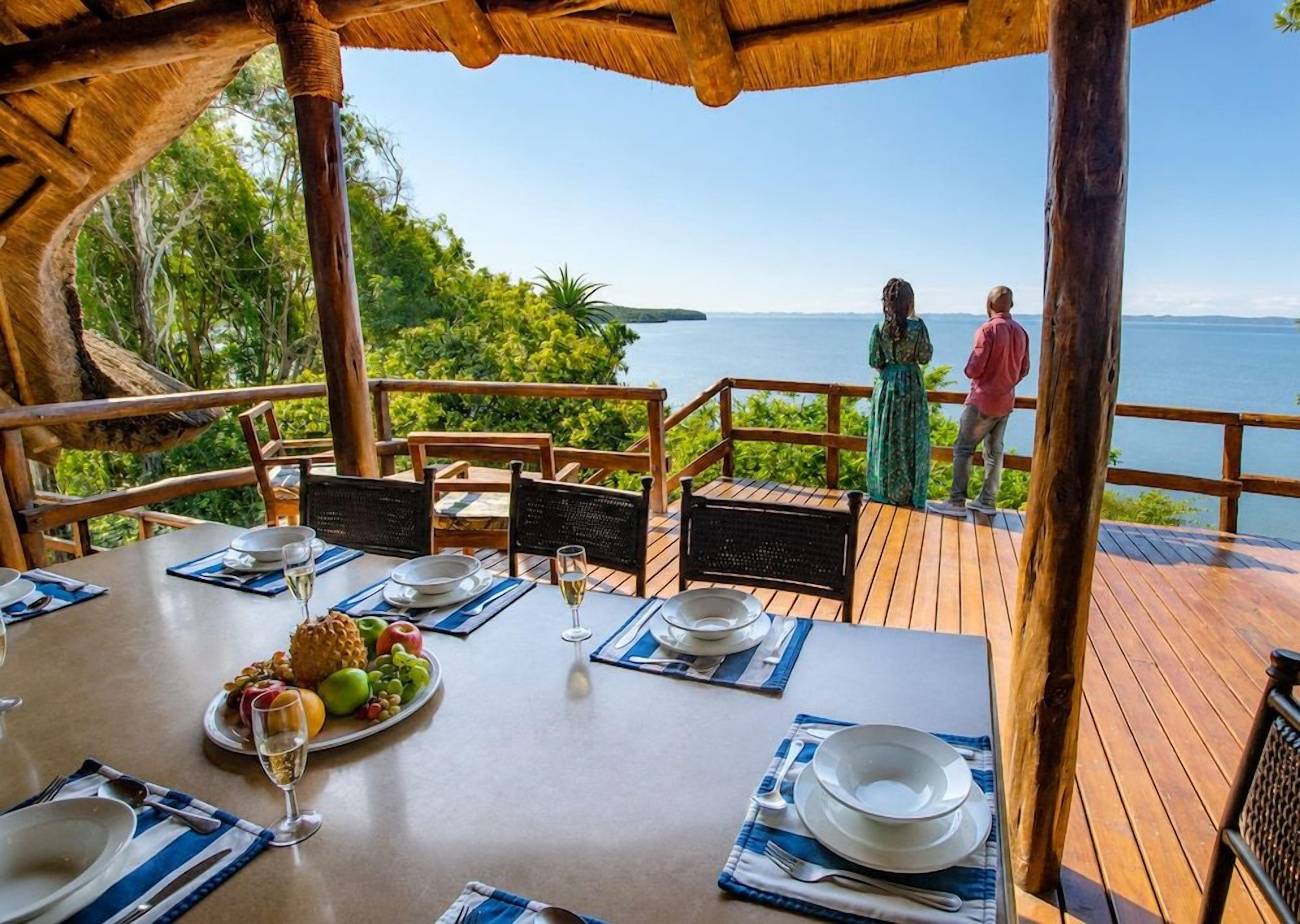 Un área de comedor con una mesa para dos, con vista a un cuerpo de agua y vegetación.