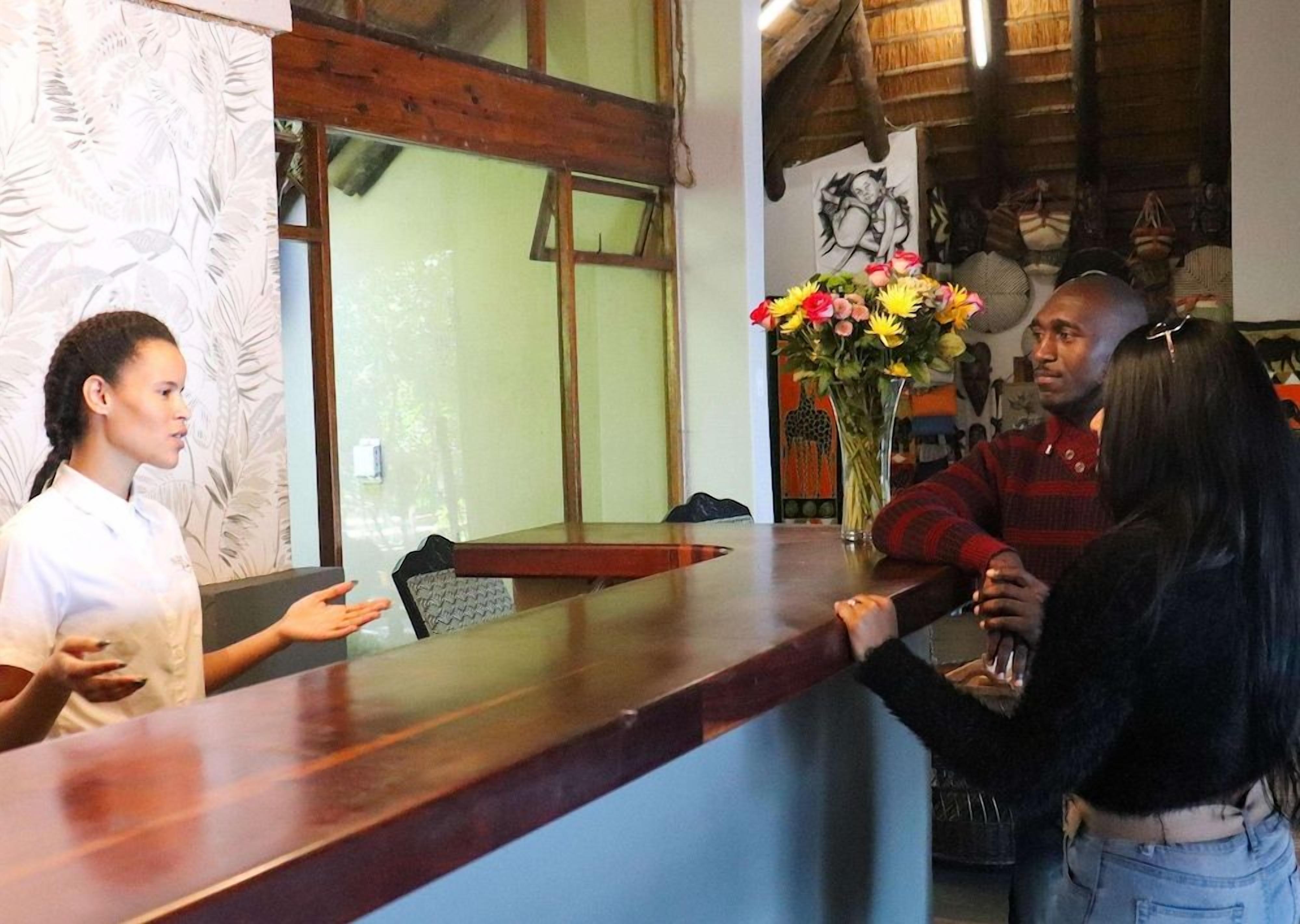 Un área de recepción con un mostrador de madera, un jarrón de flores y un mural en la pared.