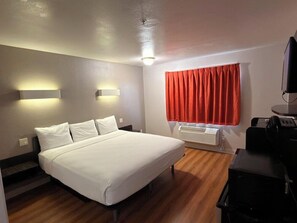 A hotel room with a bed, a desk, a chair, a television, and a window with red curtains. - Americas Best Value Inn Apache Junction (Apache Junction)