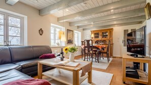 A modern living room with a sofa, coffee table, and a dining area with chairs and a table. - Westertilli 8 – Thatched-Roof House with Romantic Garden (Pellworm)