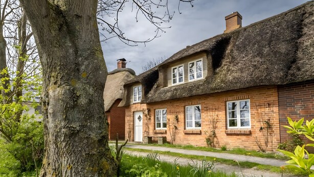 A traditional brick house with a thatched roof, a visible chimney, and a front door. - Westertilli 8 – Thatched-Roof House with Romantic Garden (Pellworm)