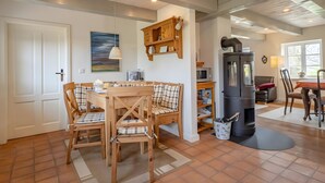 A cozy kitchen with a wooden table, chairs, a stove, and a painting on the wall. - Westertilli 8 – Thatched-Roof House with Romantic Garden (Pellworm)