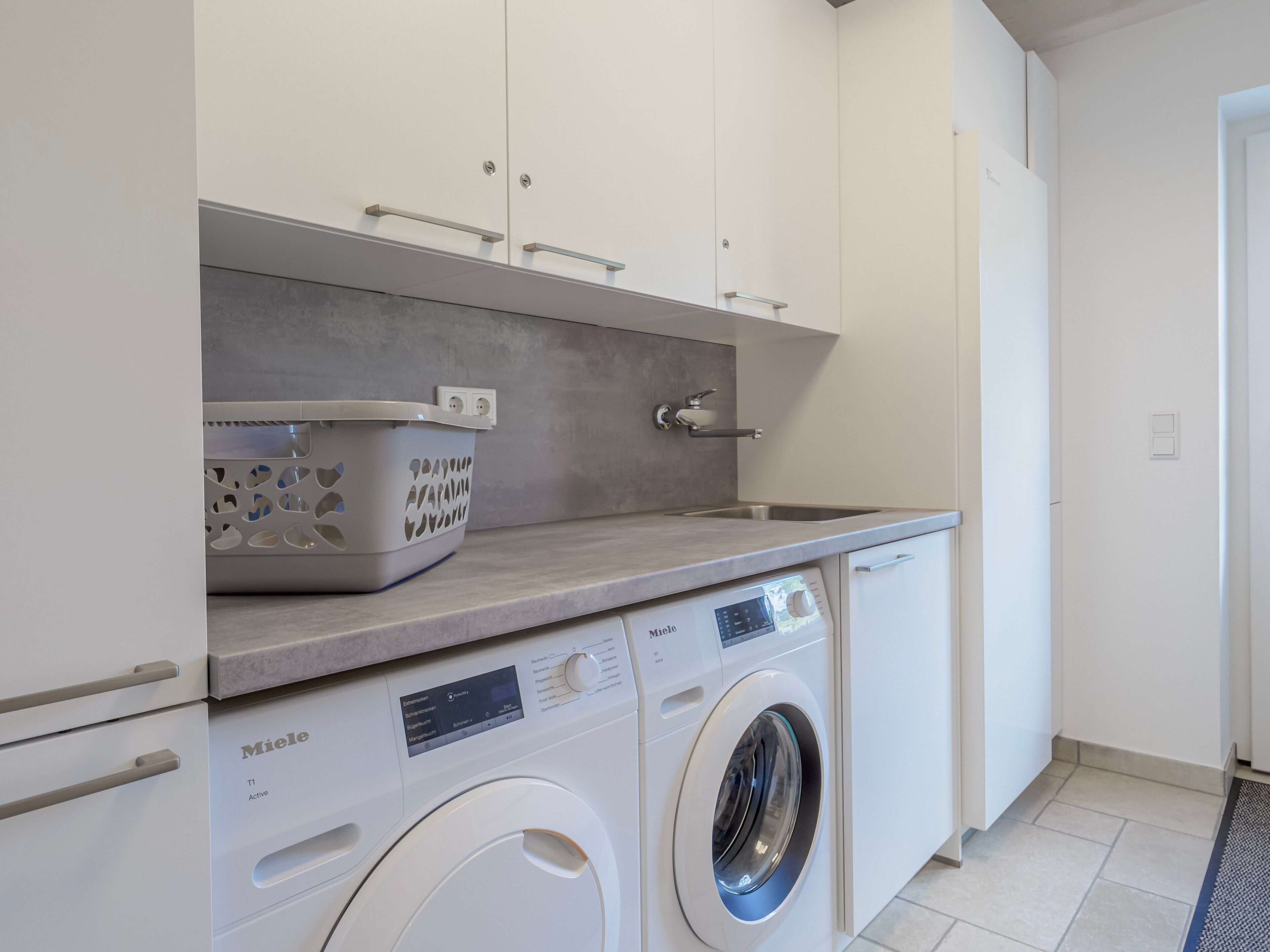 A modern laundry room with a front-loading Miele washing machine, a drying rack, and a built-in sink.
