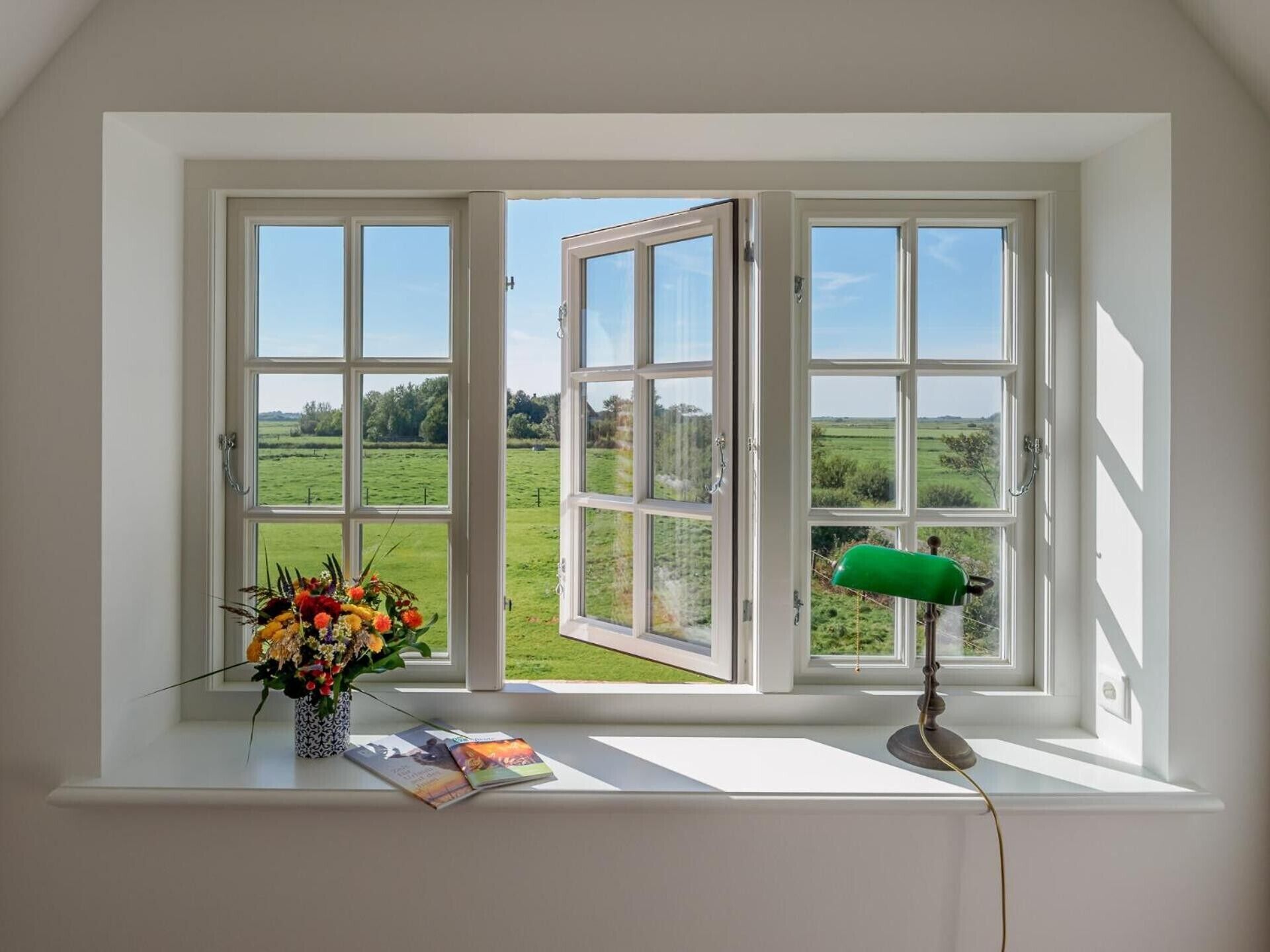 A room with a large window, a green desk lamp, and a vase of flowers on the windowsill.
