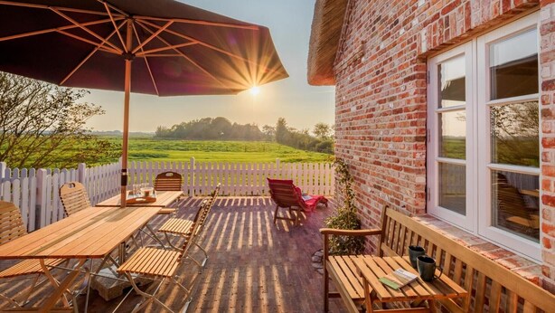 An outdoor patio with a table and chairs, a white picket fence, and a brick wall. - 5-Star Thatched Holiday Home "Emmas Hus" with Sauna and Fireplace (Pellworm)