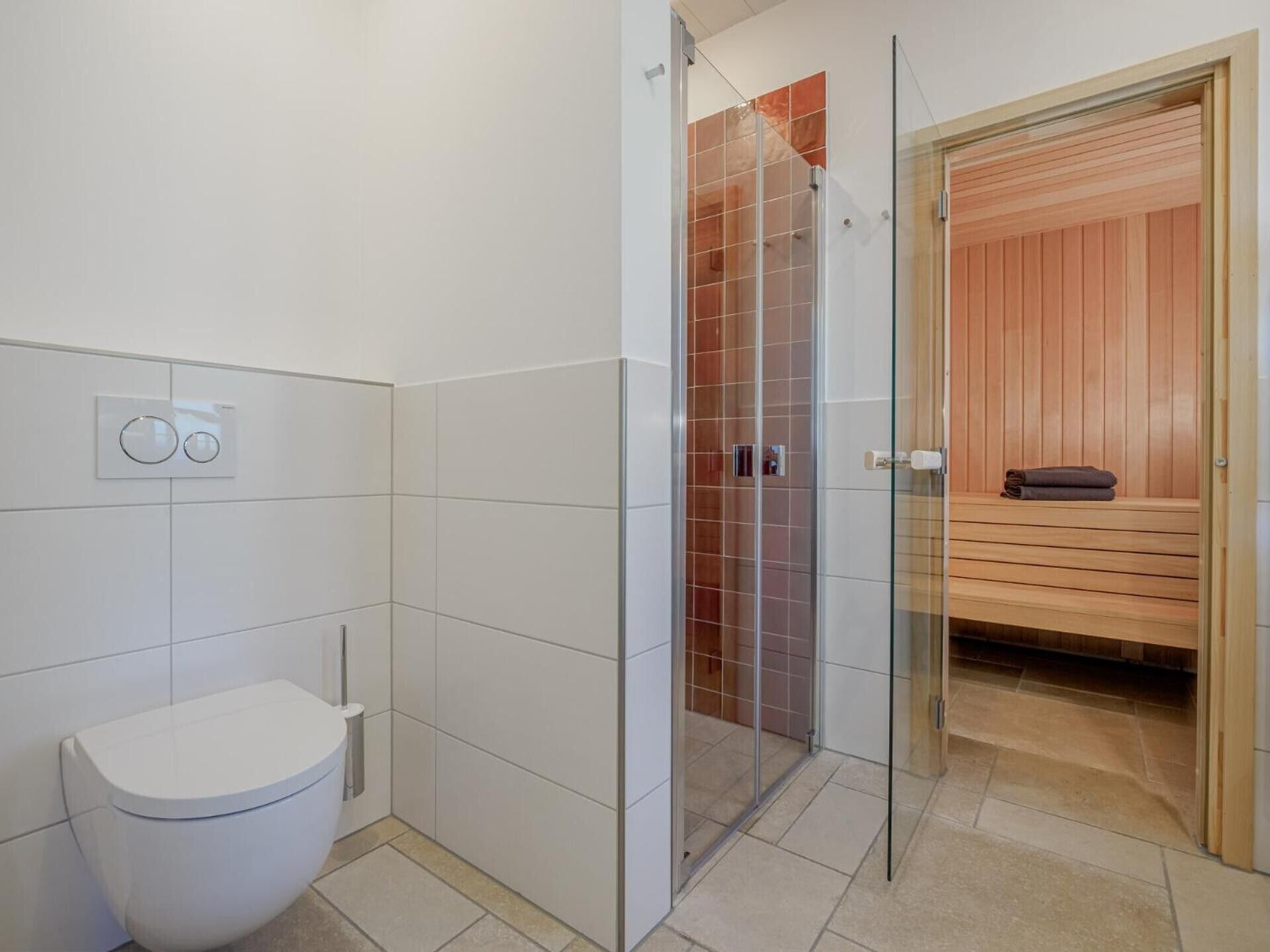 Een moderne badkamer met een douchecabine van glas, een wit toilet en een sauna zichtbaar door een glazen deur.