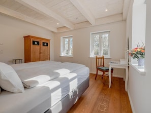 Un dormitorio con cama, armario de madera, dos ventanas, un escritorio y una silla.