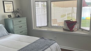 A bedroom with a bed, a dresser, a bench, a window with blinds, and a surfboard decoration.
