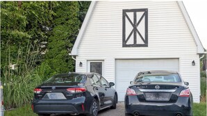 Two cars parked in front of a white building with a black X-shaped window.