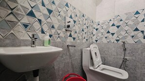 Ein Badezimmer mit Waschbecken, Toilette und Dusche. Die Wände sind mit einem geometrischen Muster gefliest.