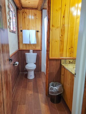 A small bathroom with a toilet, a trash bin, and wooden walls. - Grand Canyon Inn & Motel (Williams)