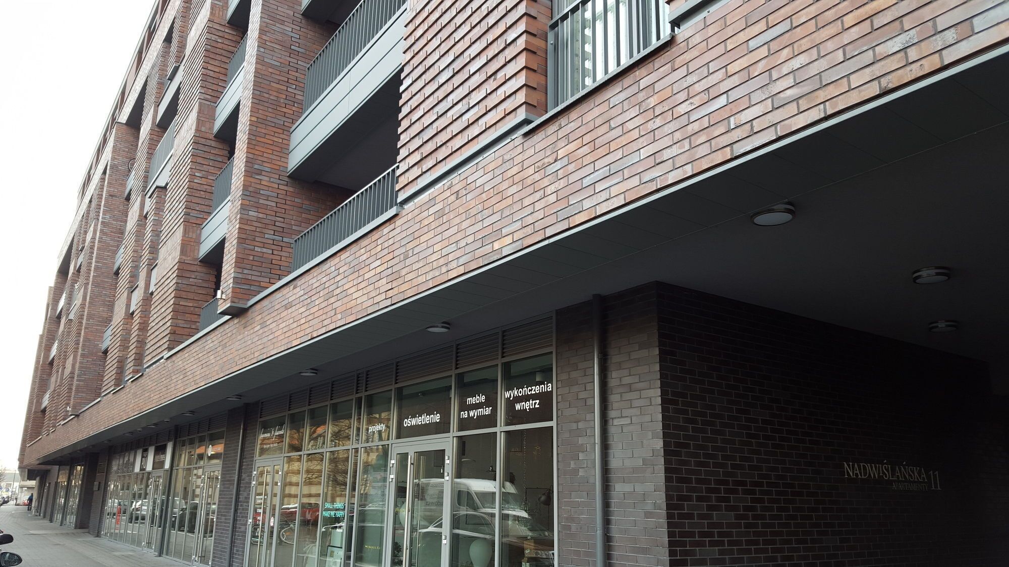 Ein modernes Gebäude mit Backsteinfassade, großen Fenstern und einem Schild, das die Adresse Nadwieslnska 11 angibt.