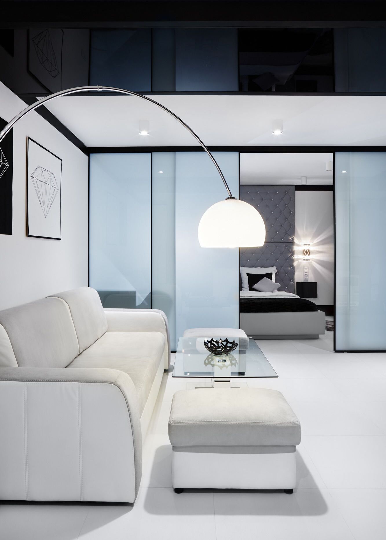 Un salon moderne avec un canapé blanc, une table basse en verre et un luminaire suspendu.
