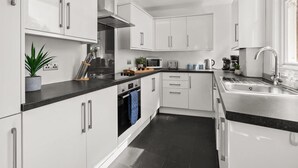 Uma cozinha moderna com armários brancos, eletrodomésticos de aço inoxidável e bancada preta.