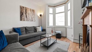 Uma sala de estar moderna com um sofá cinzento, uma mesa de centro e um grande quadro abstrato na parede.