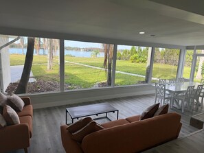 A modern living room with a large window overlooking a grassy area and a body of water. - Luxurious house on the lake for 10 ppl. (Orlando)