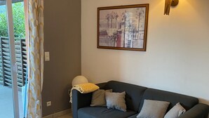 Uma sala de estar com um sofá cinza escuro, uma mesa de centro redonda, uma luminária de parede e uma imagem emoldurada de uma paisagem urbana.