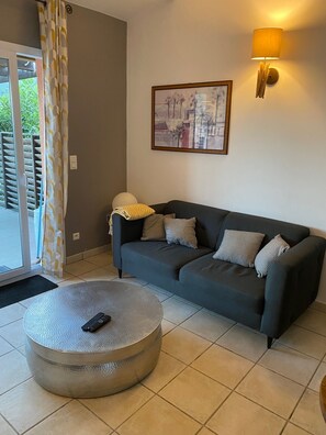 A living room with a dark grey sofa, a round coffee table, a wall-mounted lamp, and a framed cityscape picture. - Villa Lume di Corsica in Porto-Vecchio, air-conditioned, swimming pool, near Palombaggia (Porto-Vecchio)