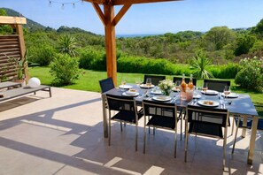 An outdoor dining area with a table set for two, surrounded by chairs, with a view of a lush landscape and a wooden pergola overhead. - Villa Lume di Corsica in Porto-Vecchio, air-conditioned, swimming pool, near Palombaggia (Porto-Vecchio)
